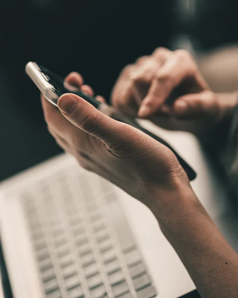 Des mains qui consultent un téléphone au-dessus d'un ordinateur portable
