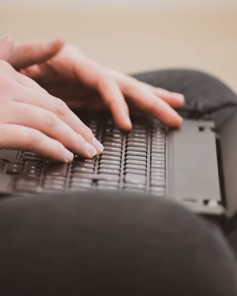 Des mains qui tapent sur un ordinateur portable posé sur les genoux